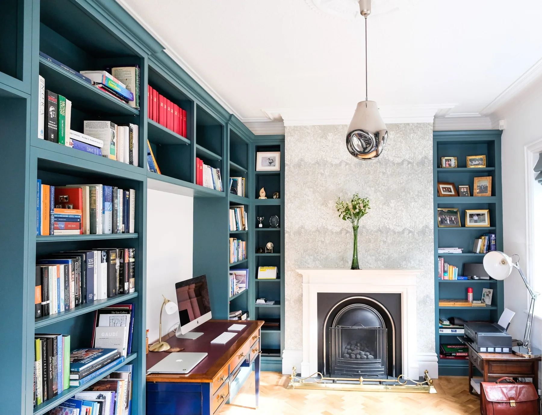 A deep green fitted library arranged around a desk and fireplace